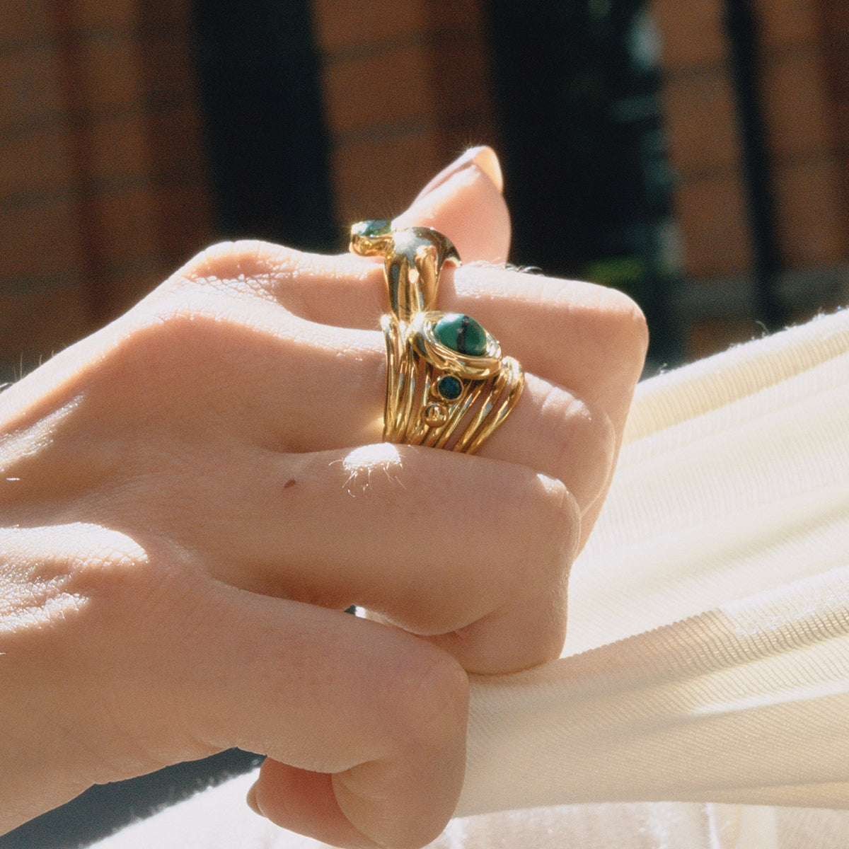 Close-up of a hand wearing gold rings with green gemstones against a blurred background