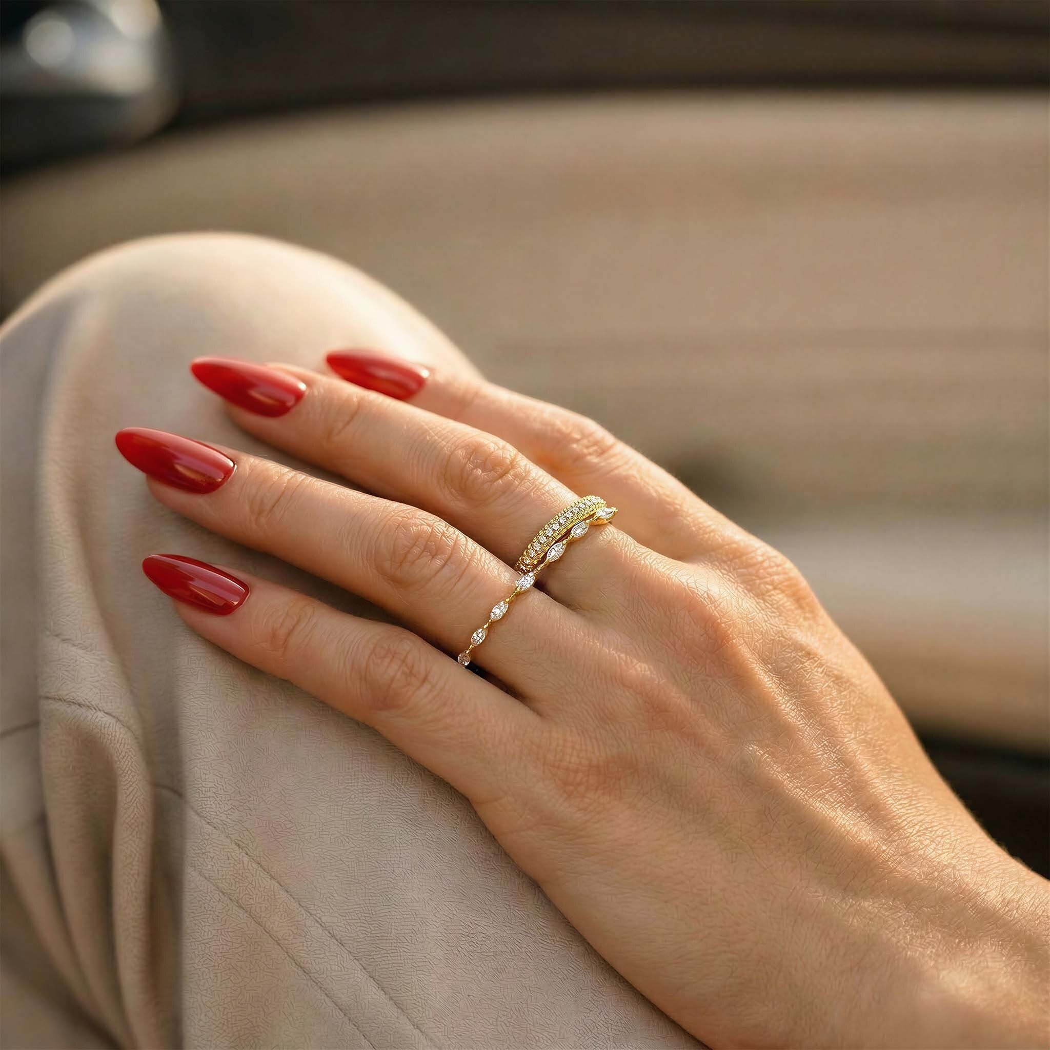 Hand with red nail polish wearing a gold ring on a beige surface