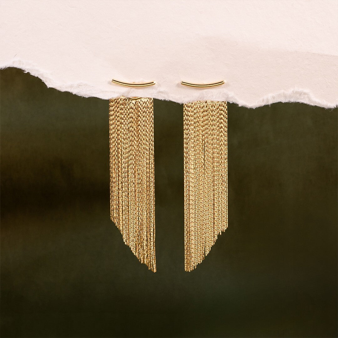 Gold chain earrings hanging from a torn white paper background