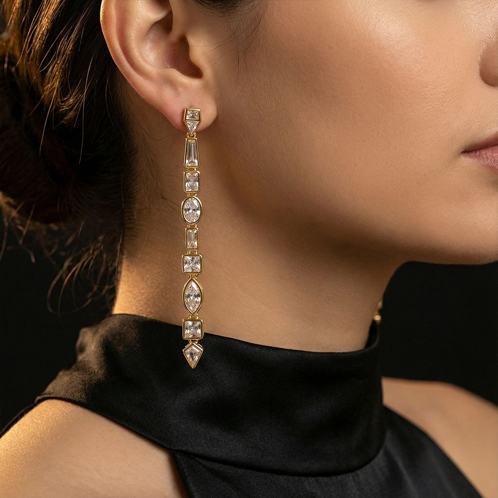 Close-up of a woman wearing gold earrings with clear stones against a blurred background.