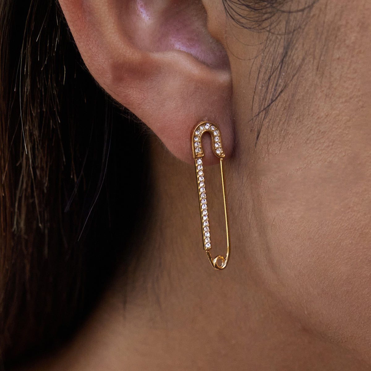 Gold safety pin earring  for women with clear stones worn by a person.