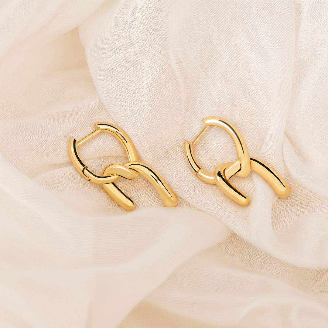 Gold earrings for women on a soft beige fabric background