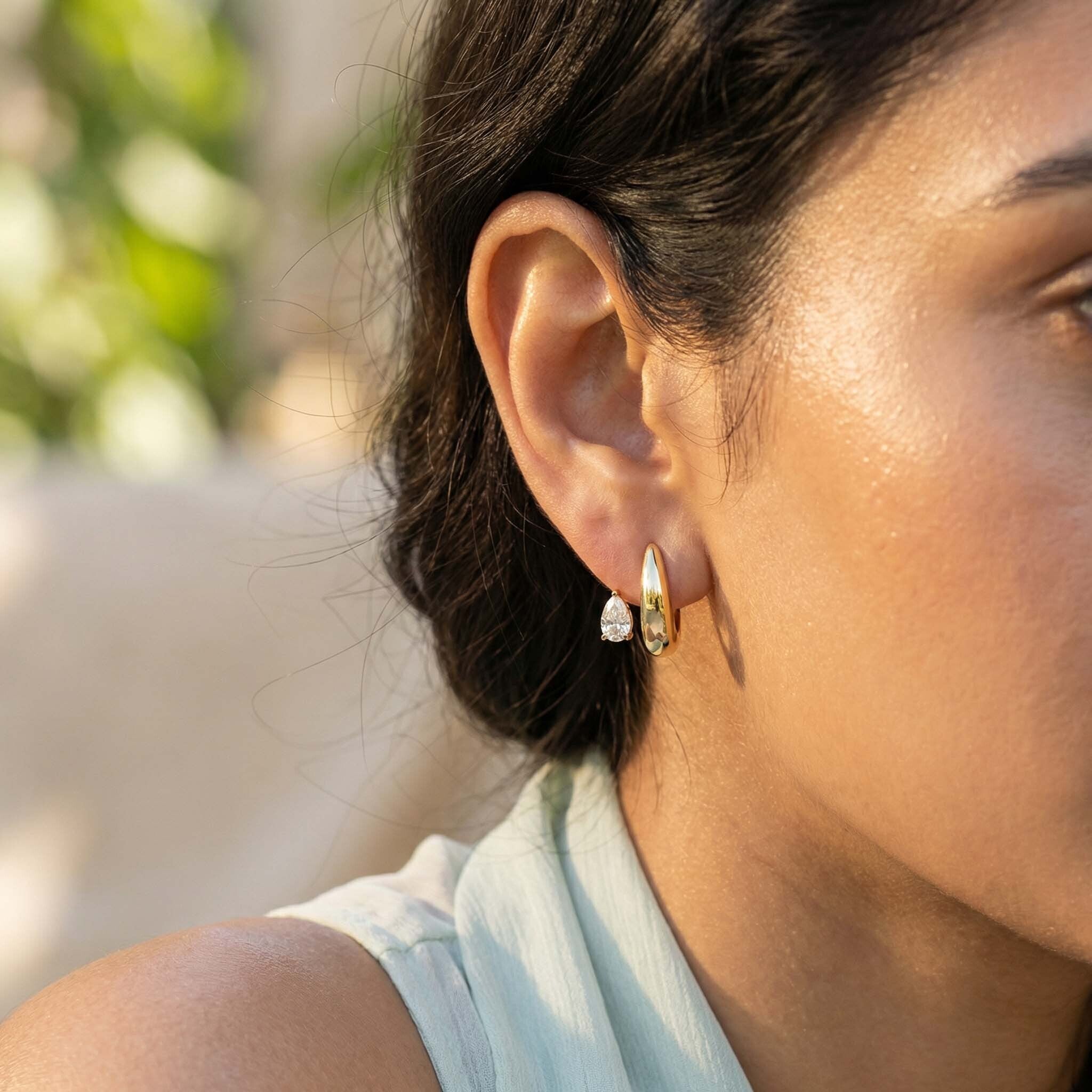 Close-up of a person wearing gold hoop earrings with a blurred natural background