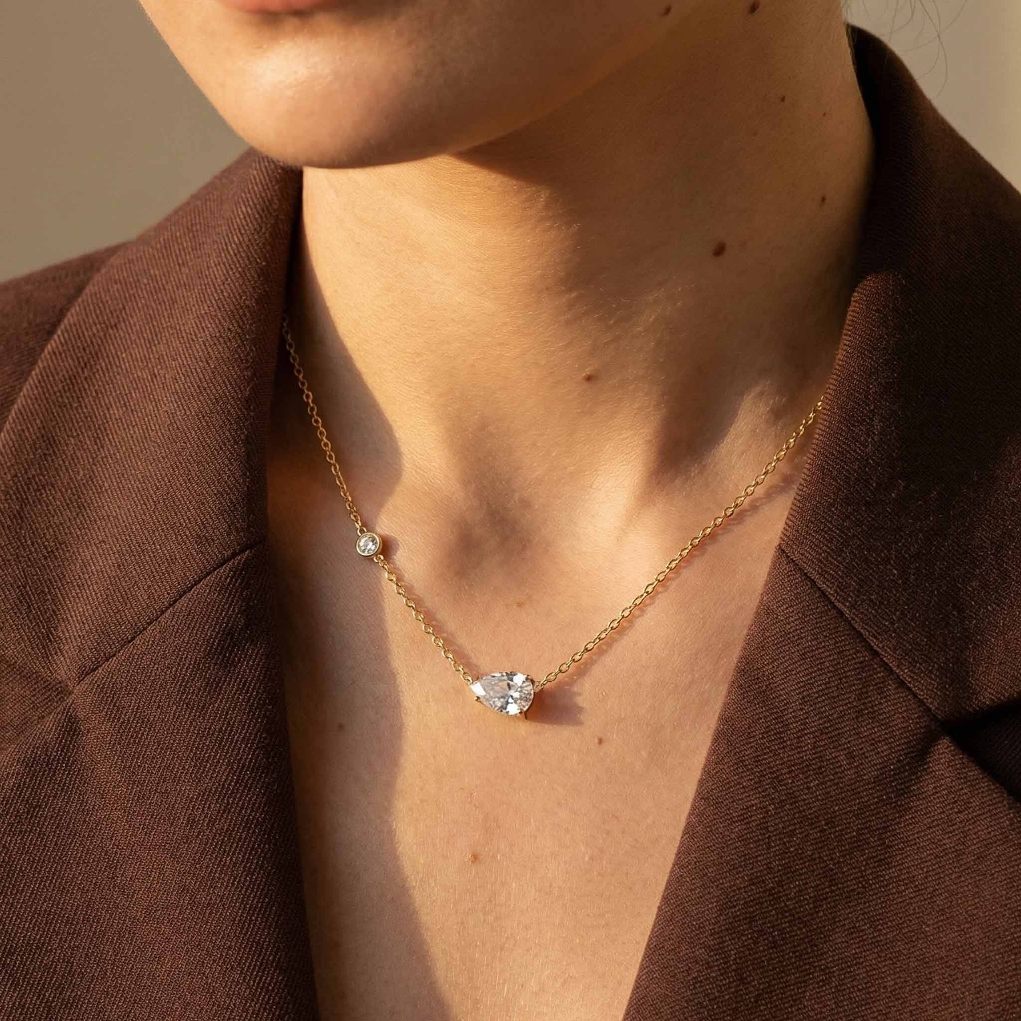 Necklace with a heart-shaped pendant worn by a person in a brown jacket.