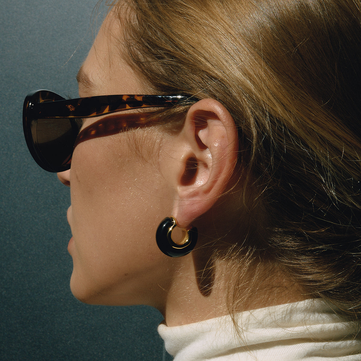 Close-up of a person wearing tortoiseshell sunglasses and a gold hoop earring.