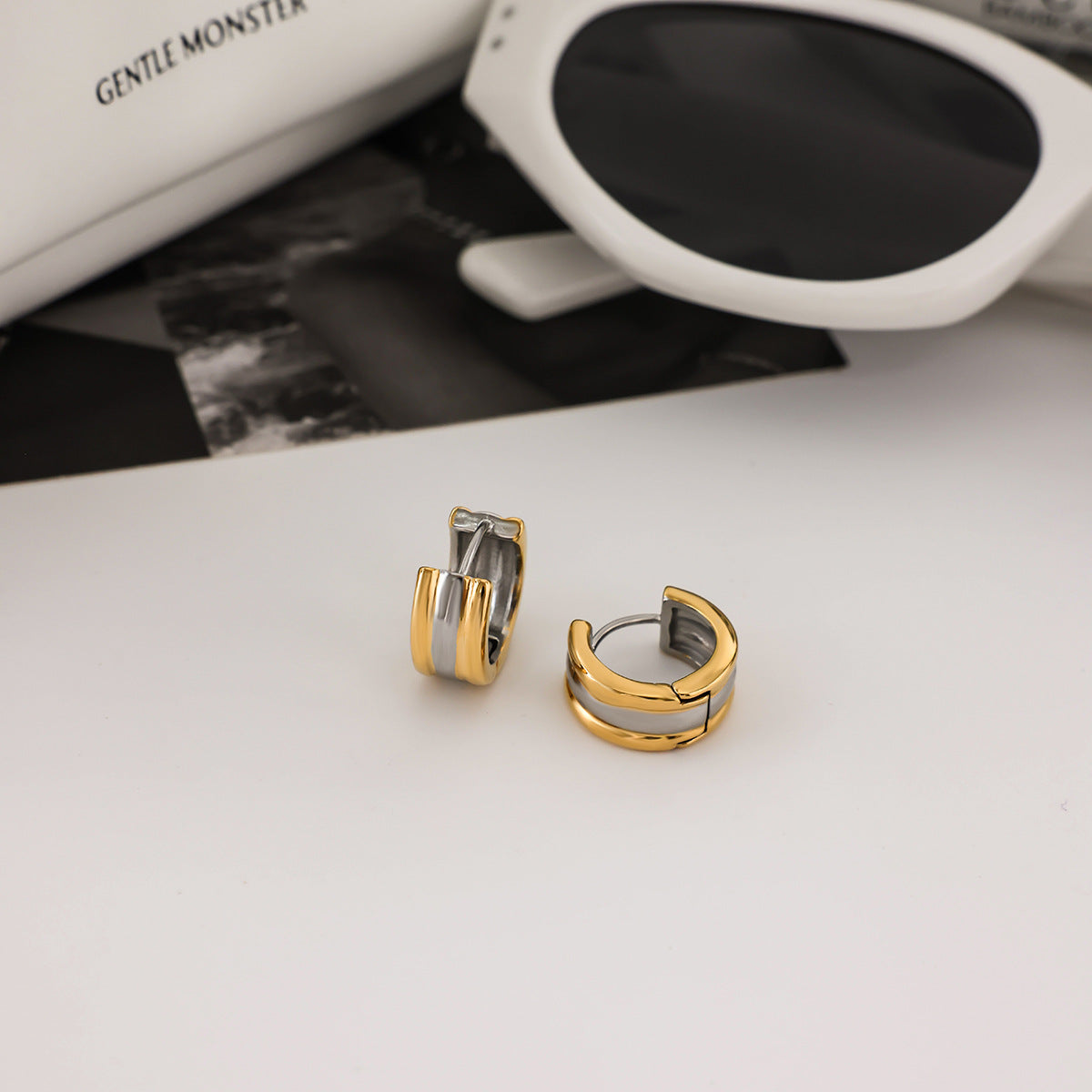 Gold and silver hoop earrings for women on a light surface with sunglasses and a bag in the background.