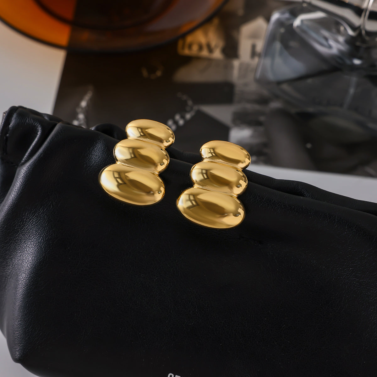 Gold earrings for women held by a black gloved hand against a blurred background