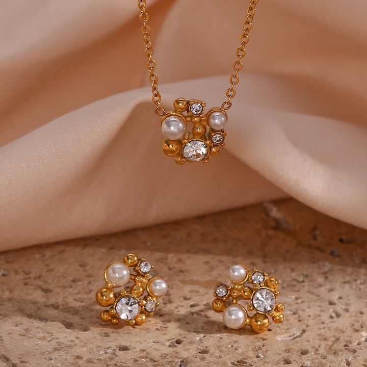 Gold necklace and earrings with pearls and crystals on a beige surface