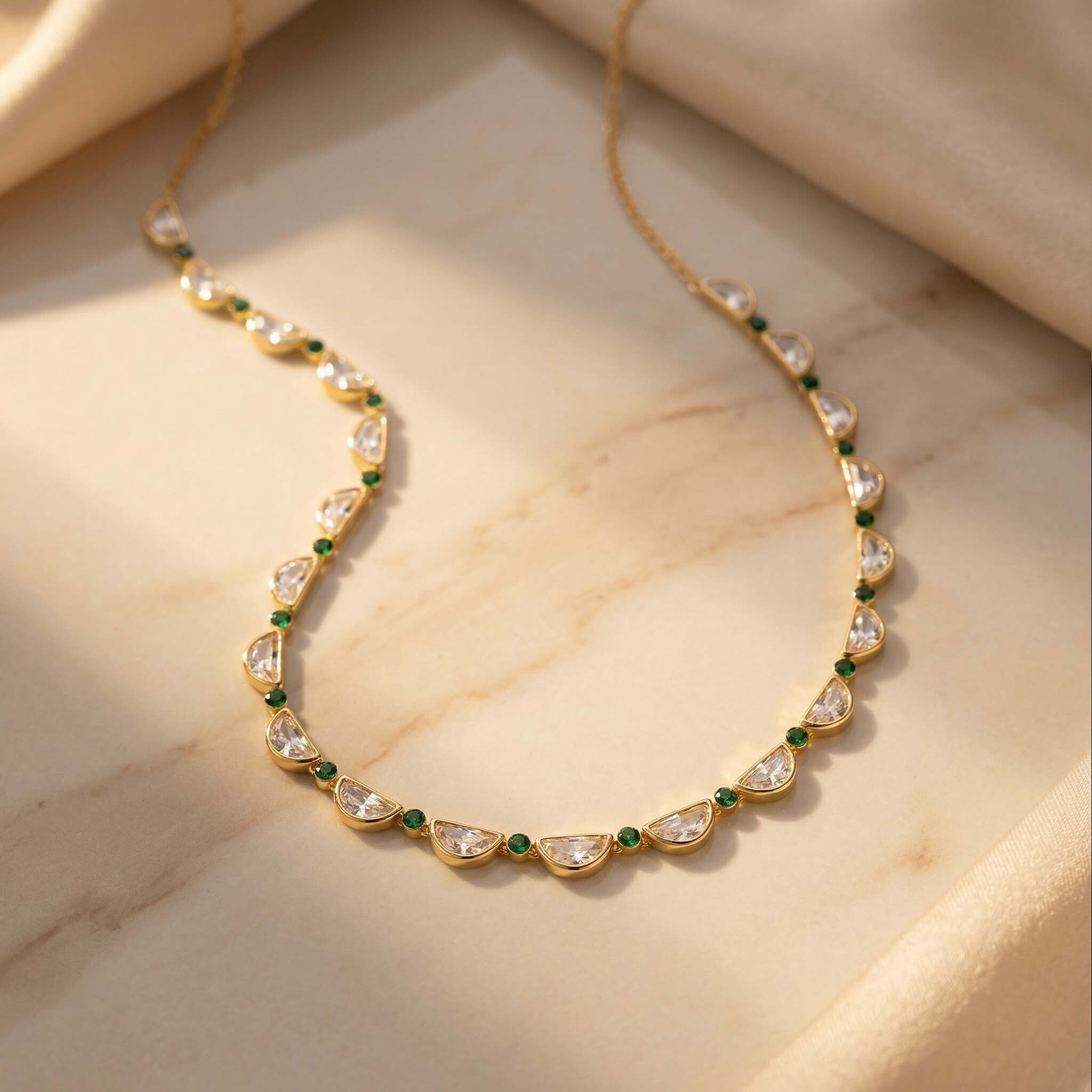 Gold necklace with green and clear stones on a beige marble surface