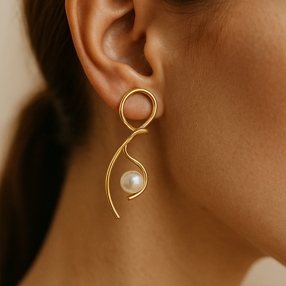 Gold earring with a pearl on an ear against a neutral background