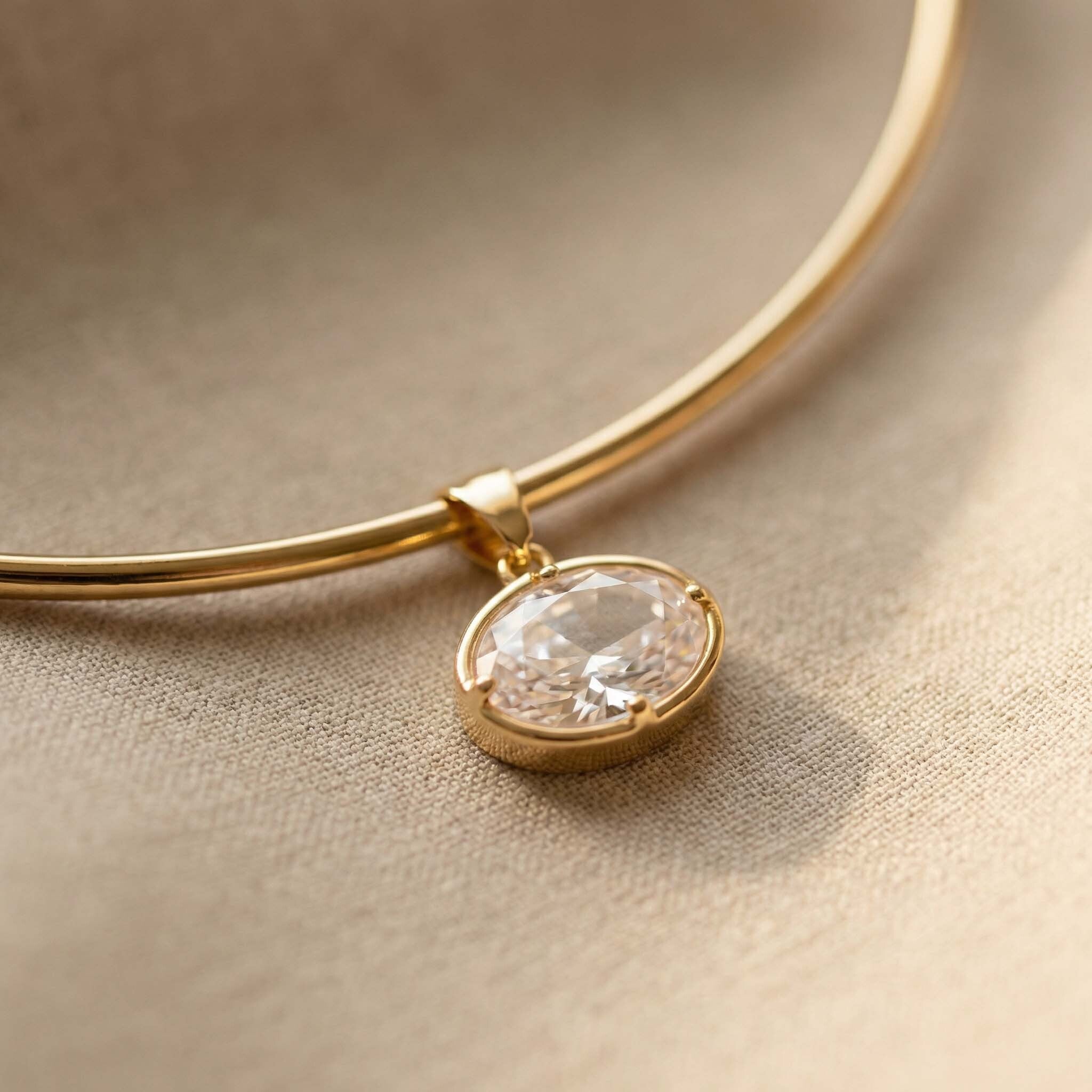 Gold necklace with a clear gemstone pendant on a beige fabric background