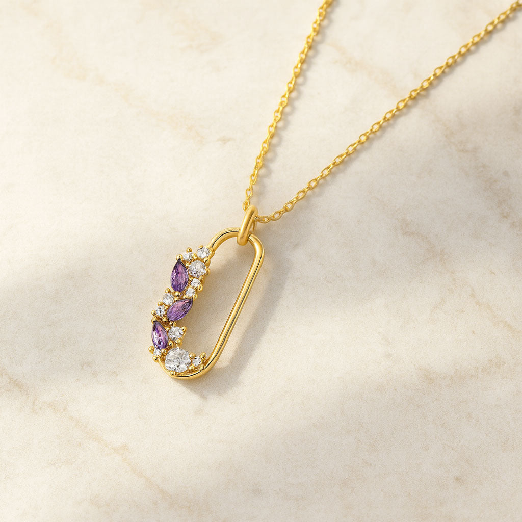 Gold necklace with purple gemstone pendant on a beige marble background