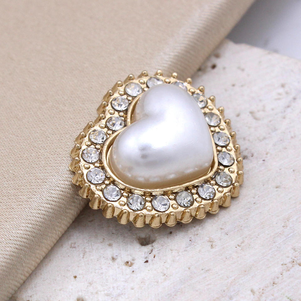Heart-shaped pearl  Button  with gold border and clear stones on a textured beige surface
