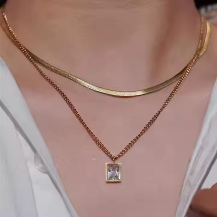 Gold necklace with a square pendant on a person wearing a white top.