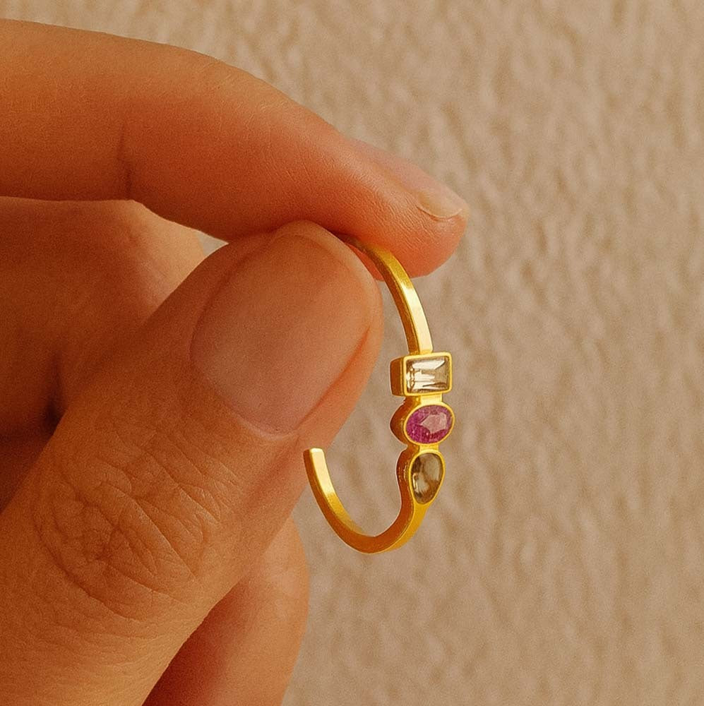 Gold hoop earring with gemstones held between fingers against a beige background