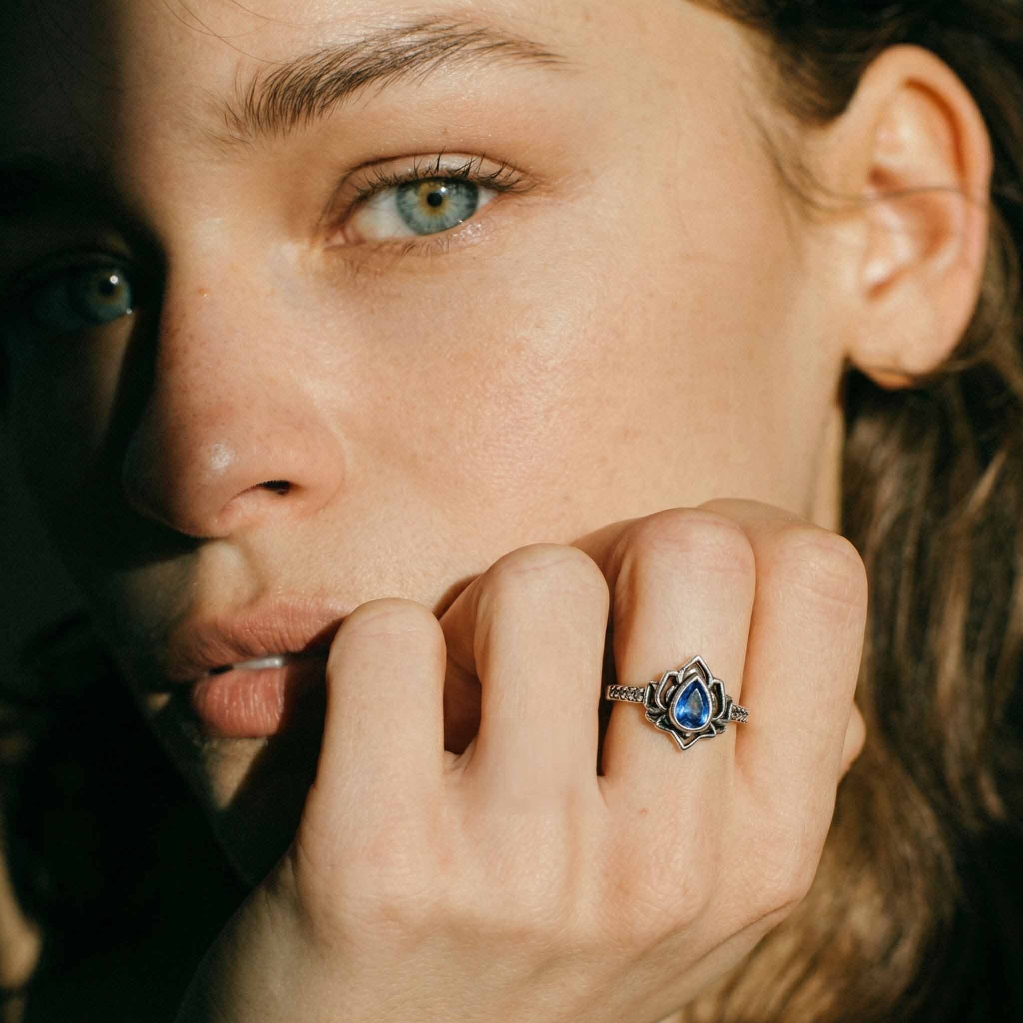 Close-up of a woman's face with a blue gemstone ring on her finger.