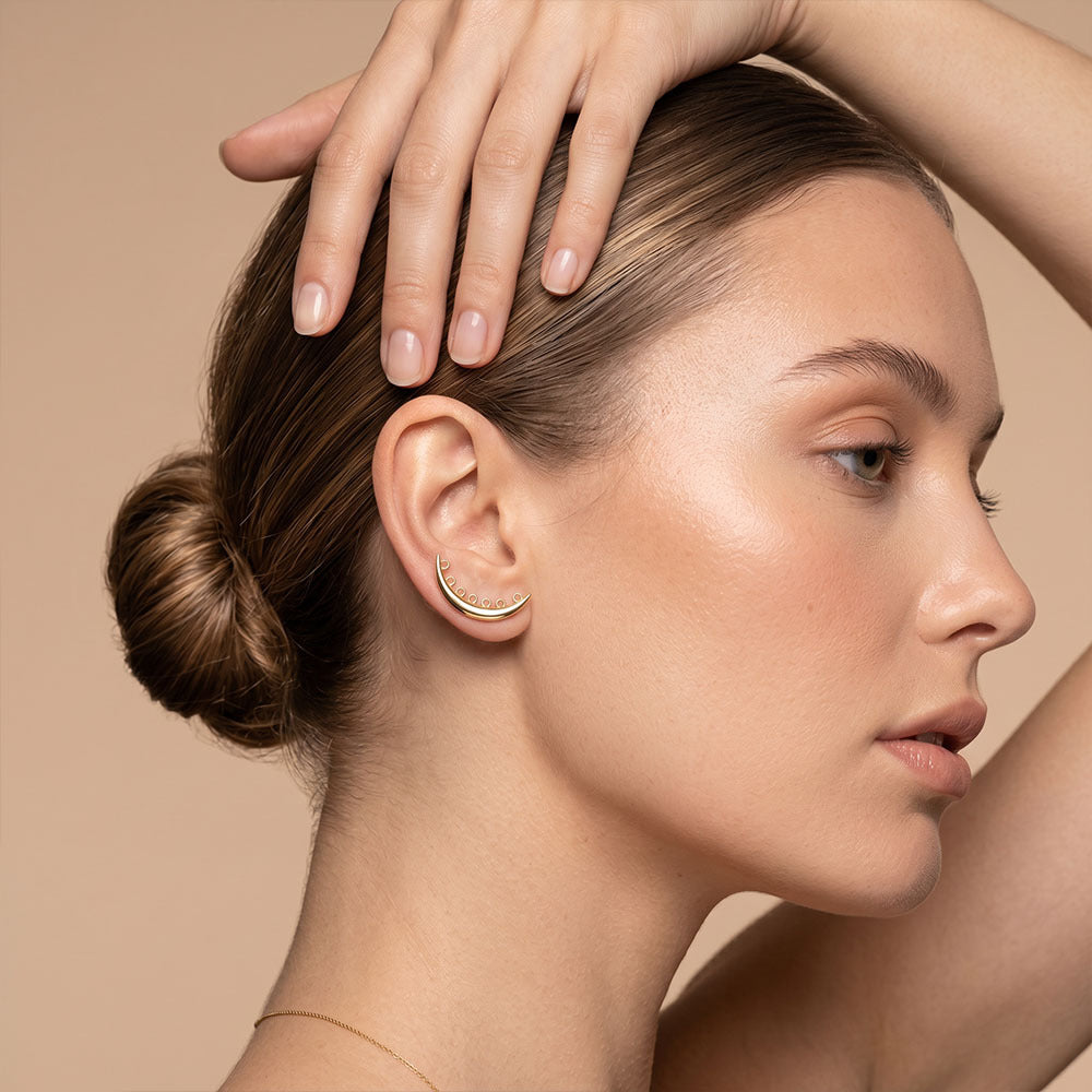 Close-up of a woman's ear with a gold earring against a beige background