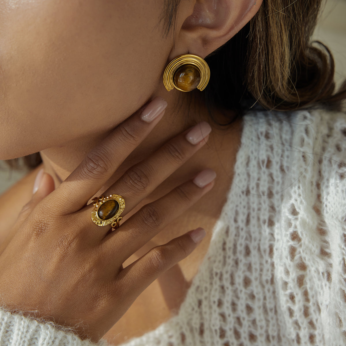 Close-up of a person wearing gold earrings  for women and ring with a white lace garment.