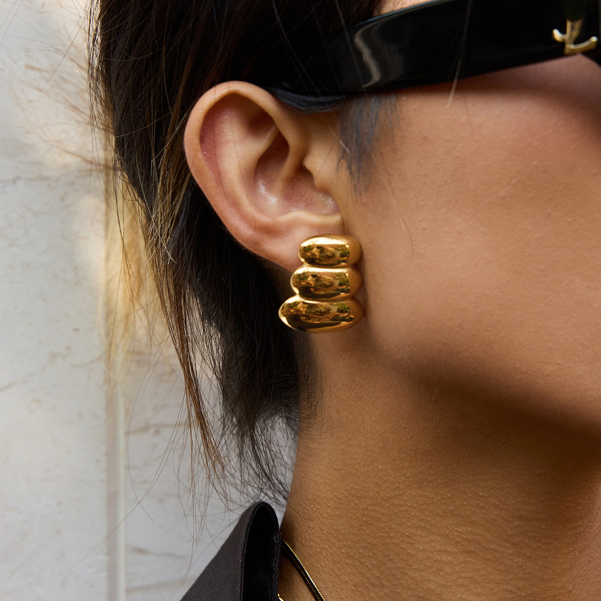 Gold  earrings for women worn by a person with a neutral background