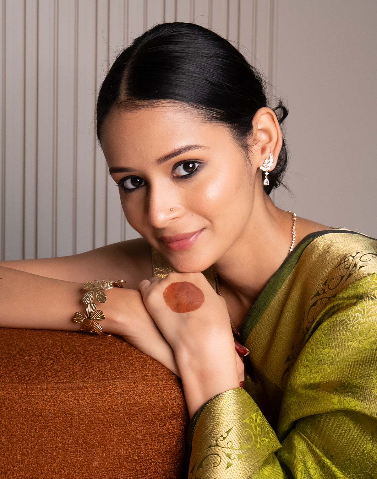 Woman in a green saree with jewelry against a neutral background