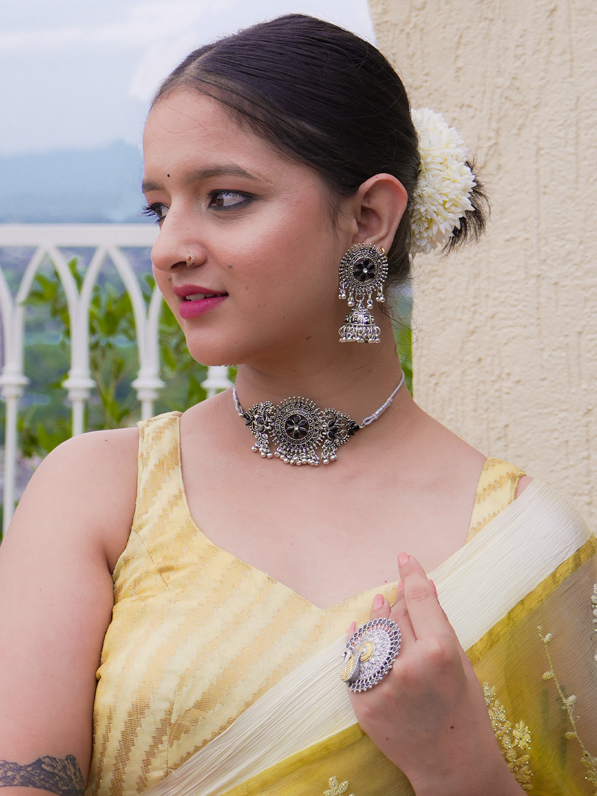 Woman wearing a yellow saree with silver jewelry against a blurred outdoor background