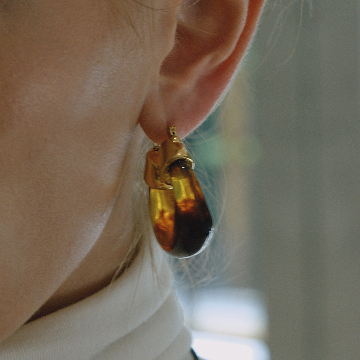 Close-up of a person wearing a gold and amber earring for women with a blurred background