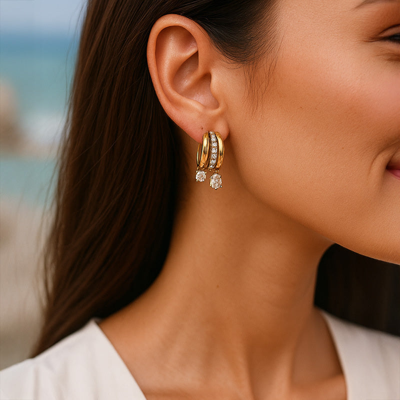 Close-up of a woman wearing gold hoop earrings with a blurred beach background