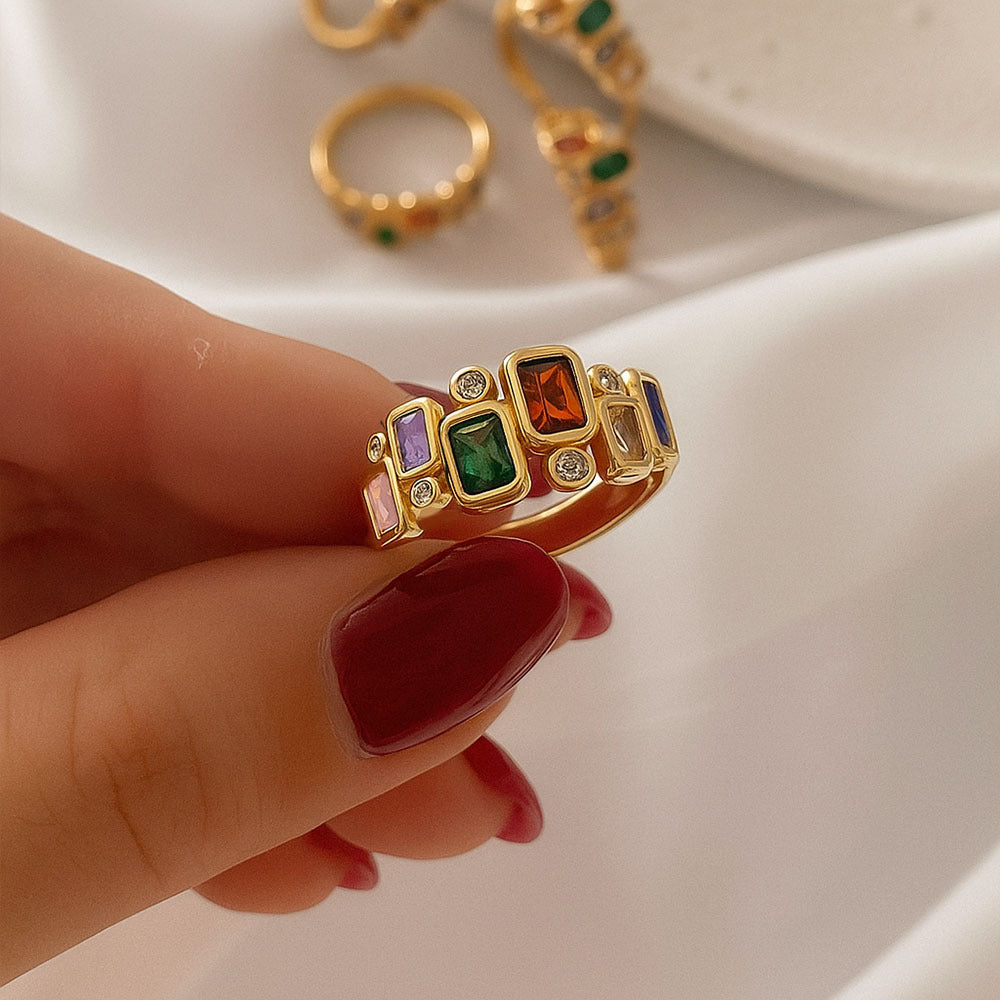 Gold ring with colorful gemstones held by a hand against a neutral background