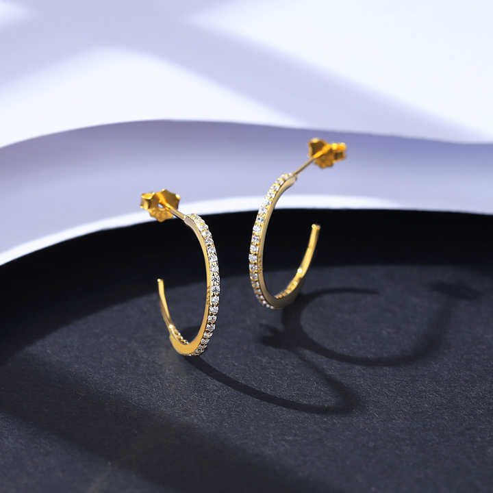 Gold hoop earrings for women with embedded stones on a dark surface