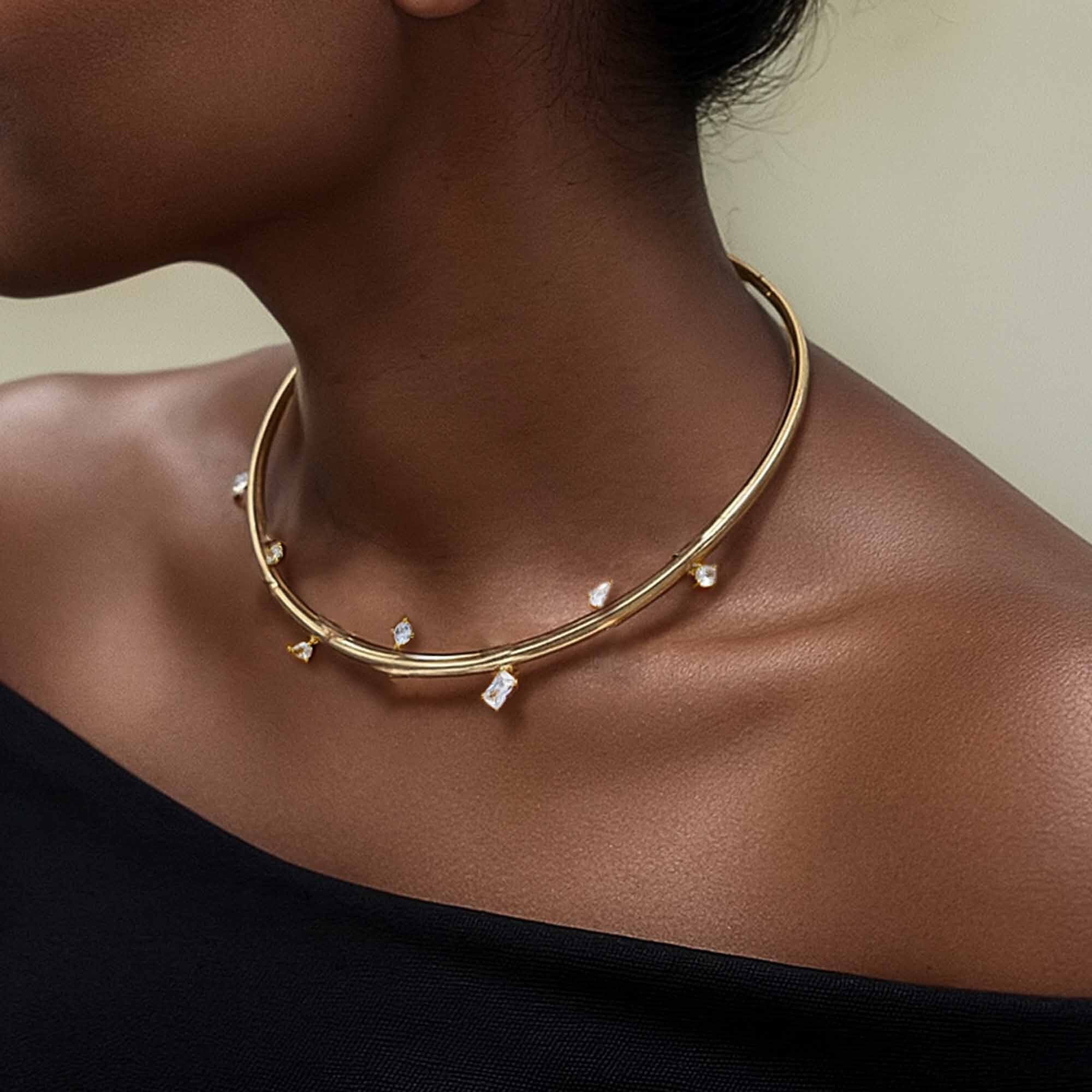 Gold necklace with small stones on a person wearing a black top.