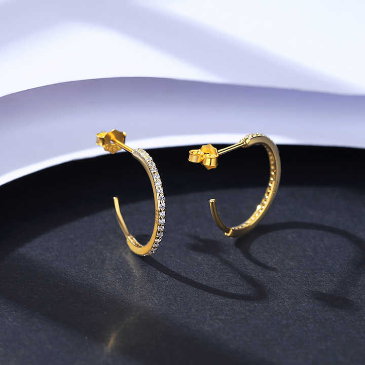 Gold hoop earrings for women with embedded stones on a dark surface