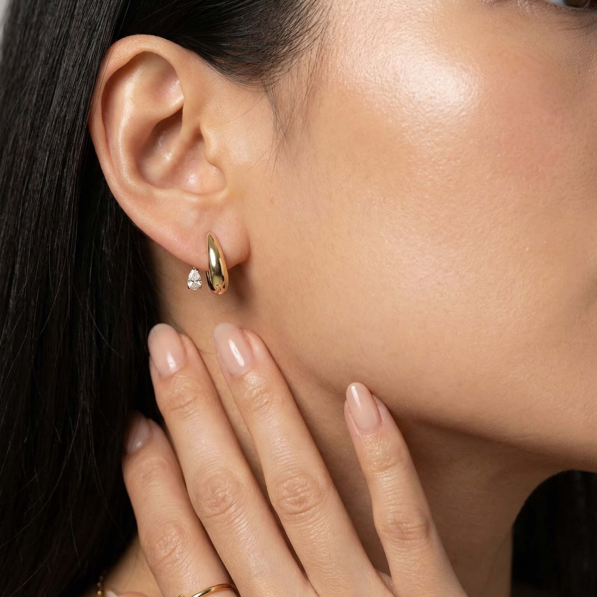 Close-up of a person wearing a gold earring with a clear gemstone.