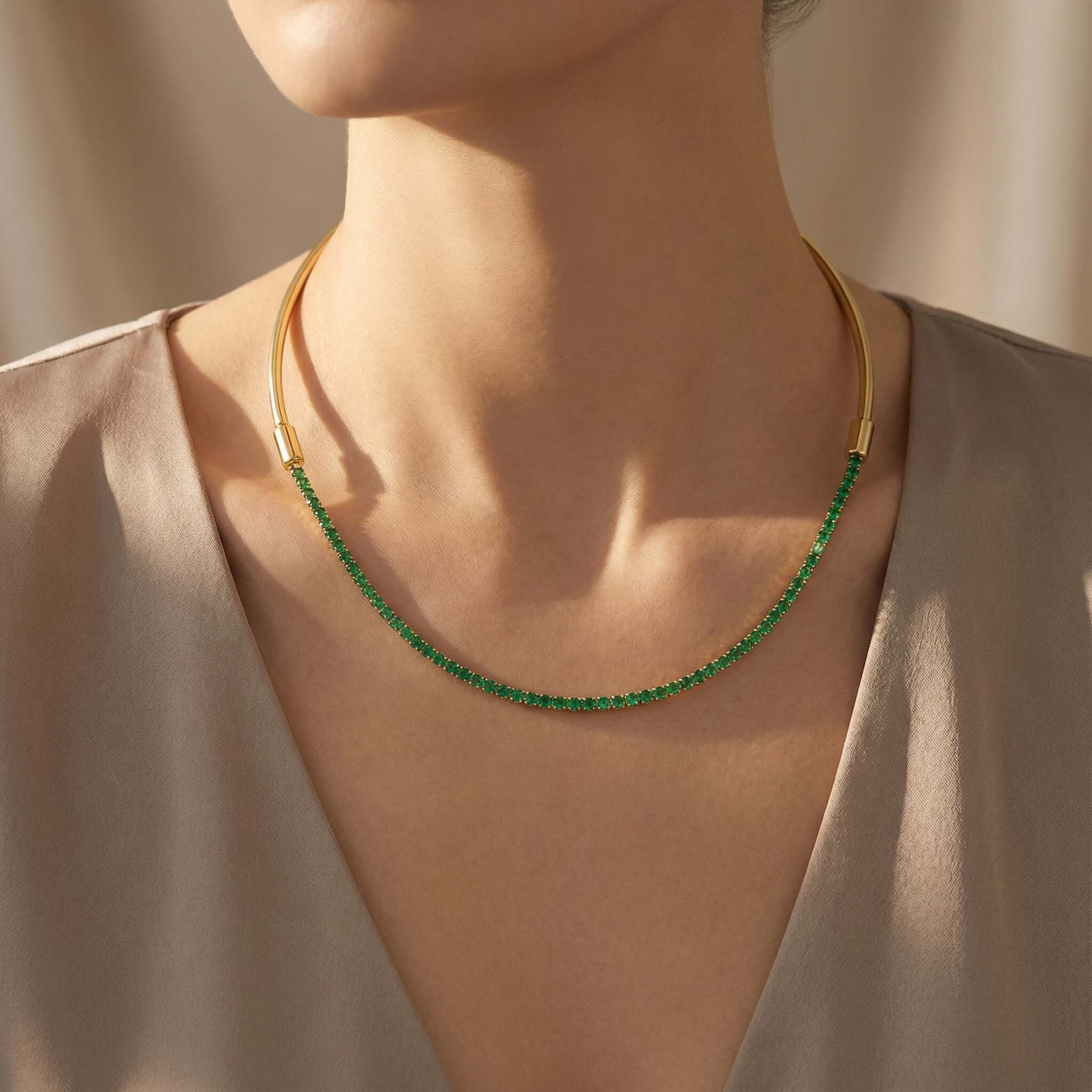 Gold necklace with green beads worn by a person against a neutral background