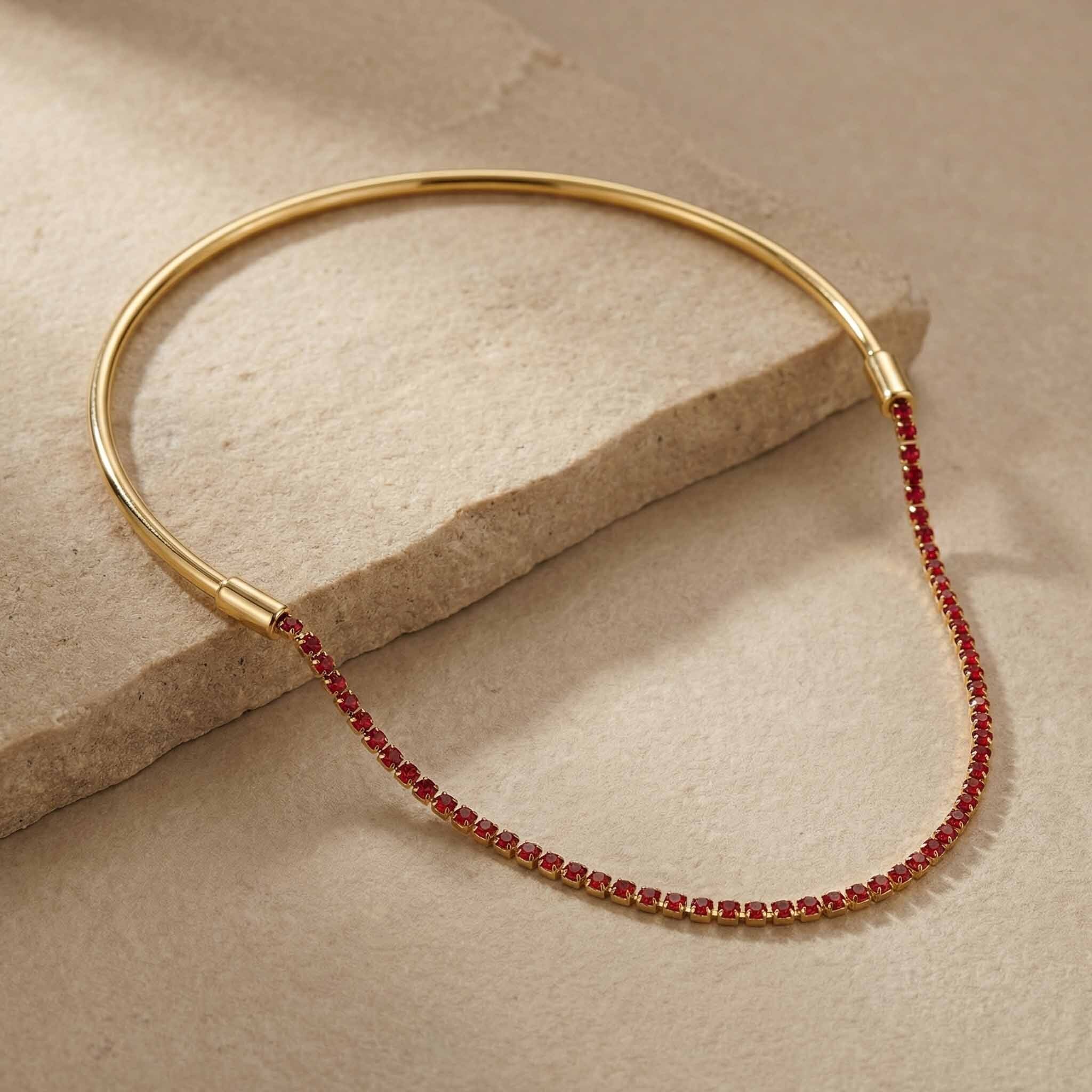 Gold bracelet with red beads on a beige stone surface