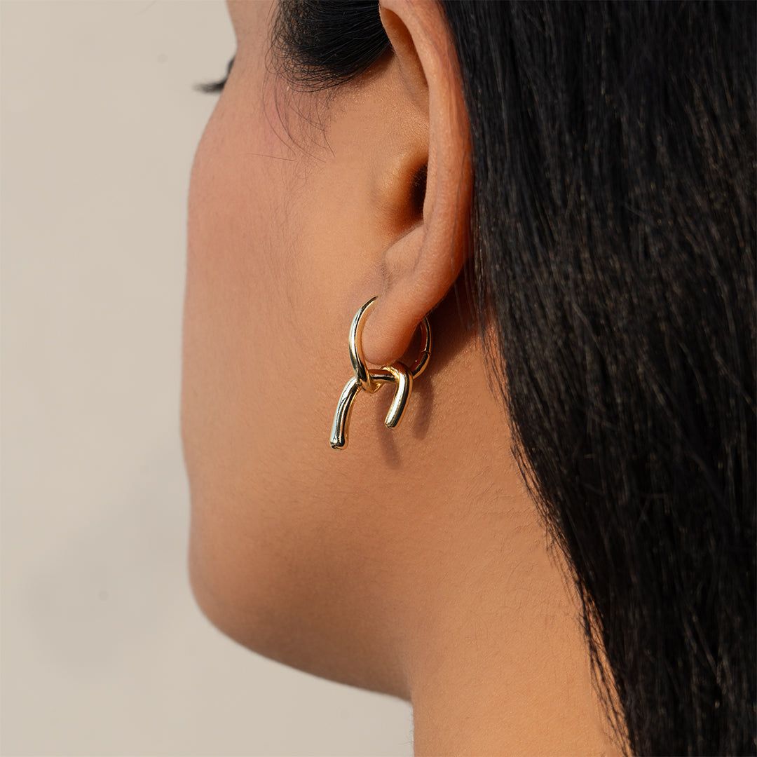 Gold hoop earrings for women worn by a person with dark hair on a neutral background