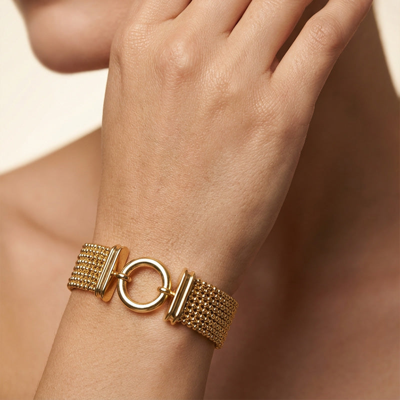 Gold bracelet on a wrist with a neutral background