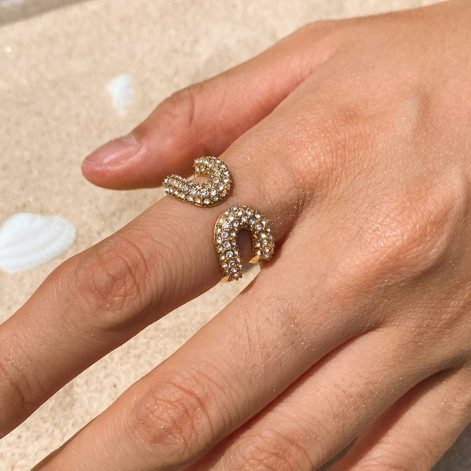 Hand wearing two gold rings with diamond accents on a neutral background