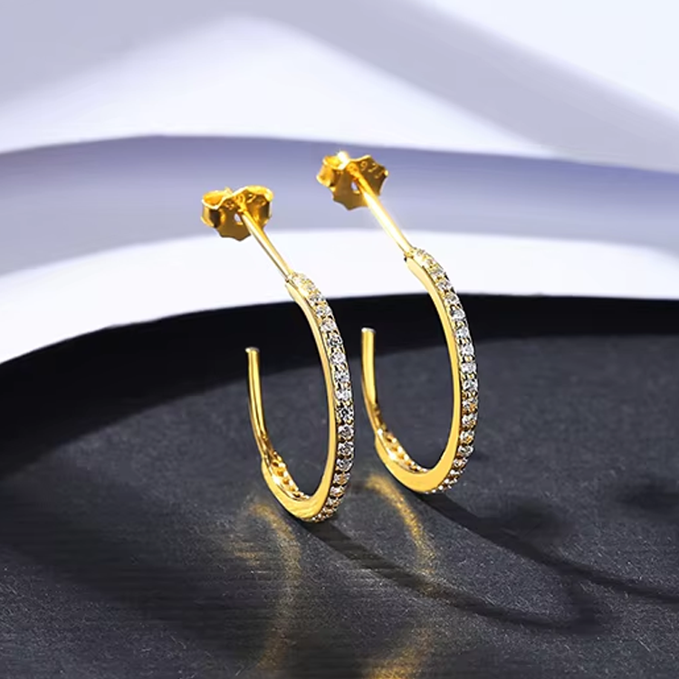 Gold hoop earrings for women with clear stones on a dark surface