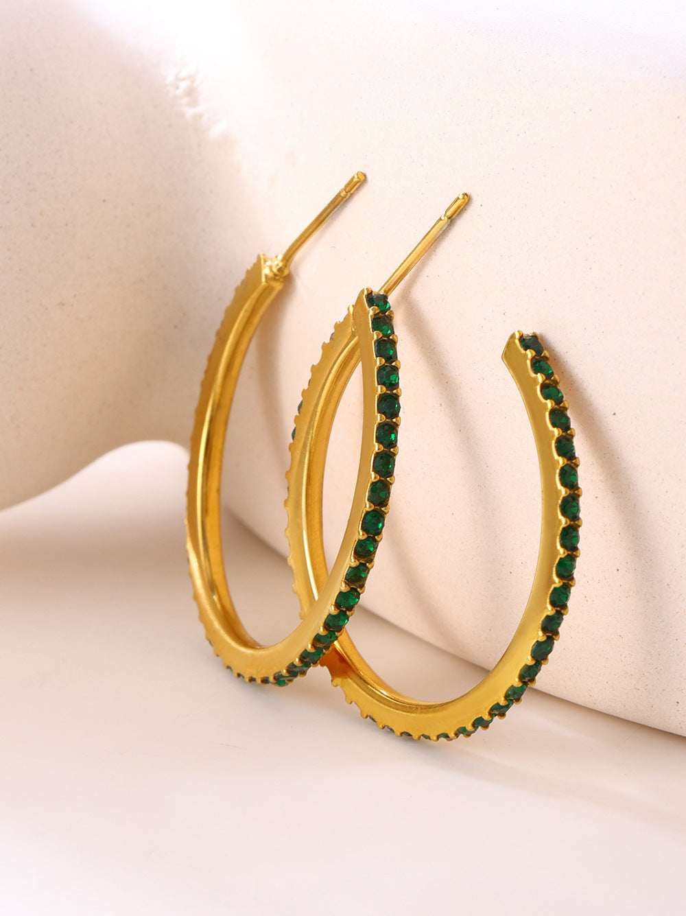 Gold hoop earrings for women with green gemstones on a beige background