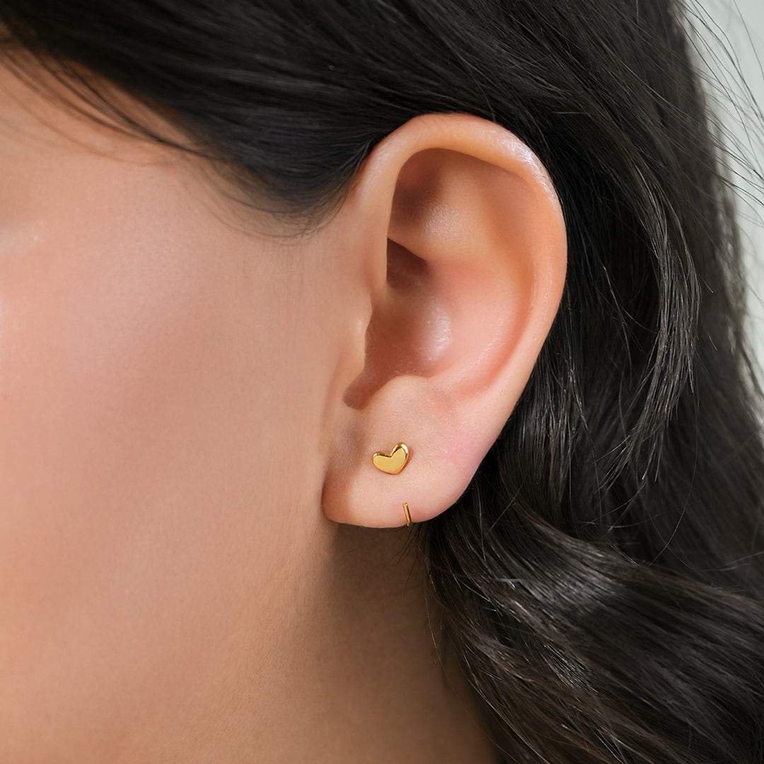 Close-up of an ear wearing a gold heart-shaped stud earrings for women  with blurred background