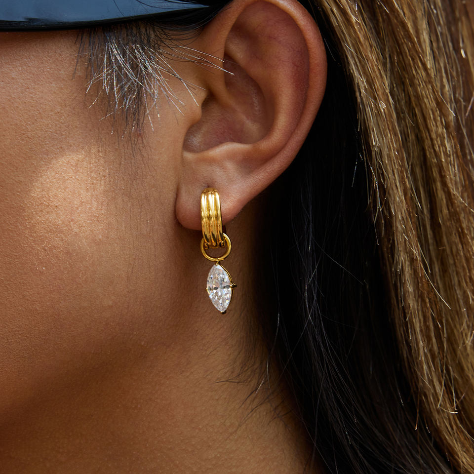 Close-up of an ear wearing a gold hoop earring with a clear gemstone.