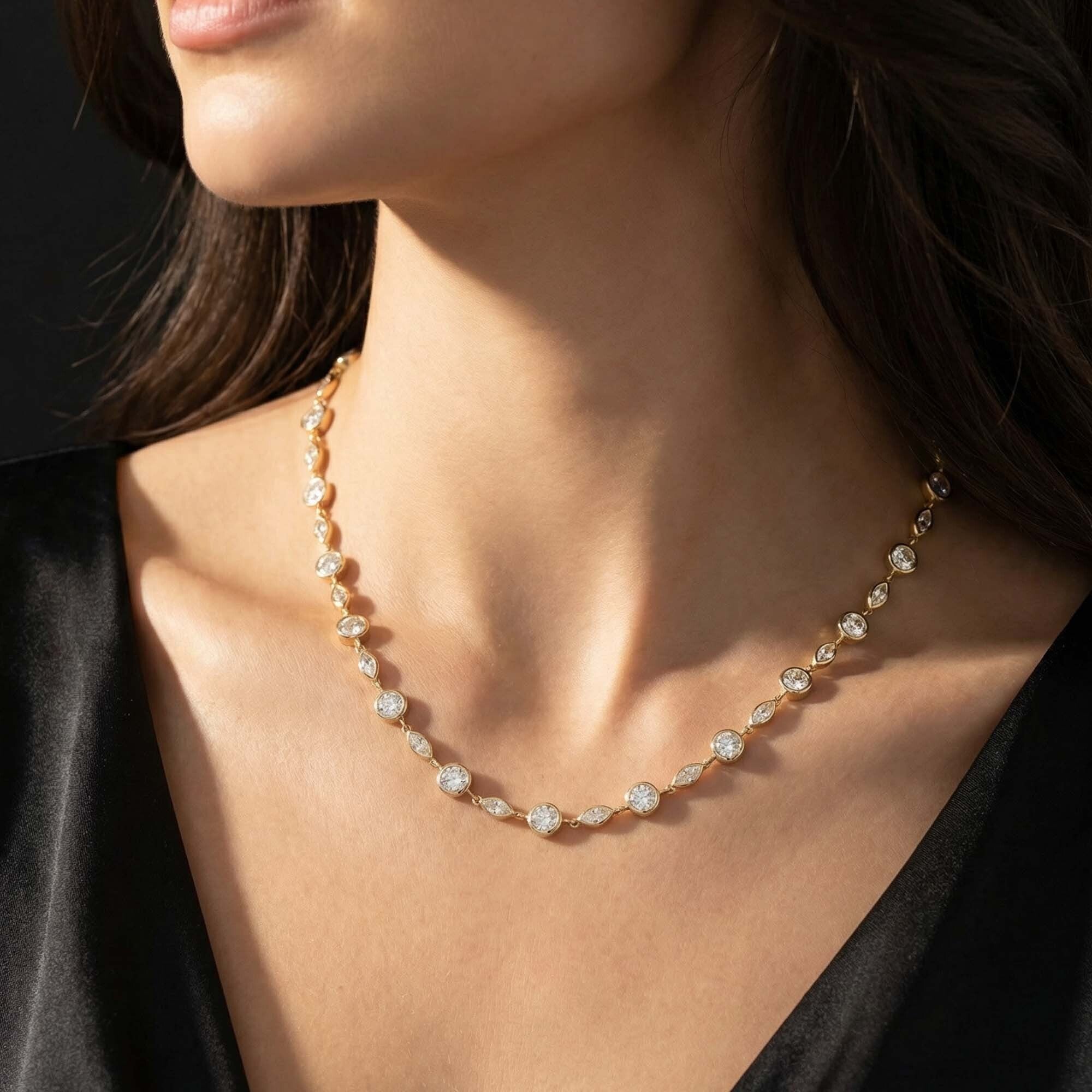 Close-up of a woman wearing a delicate gold necklace with clear stones against a dark background