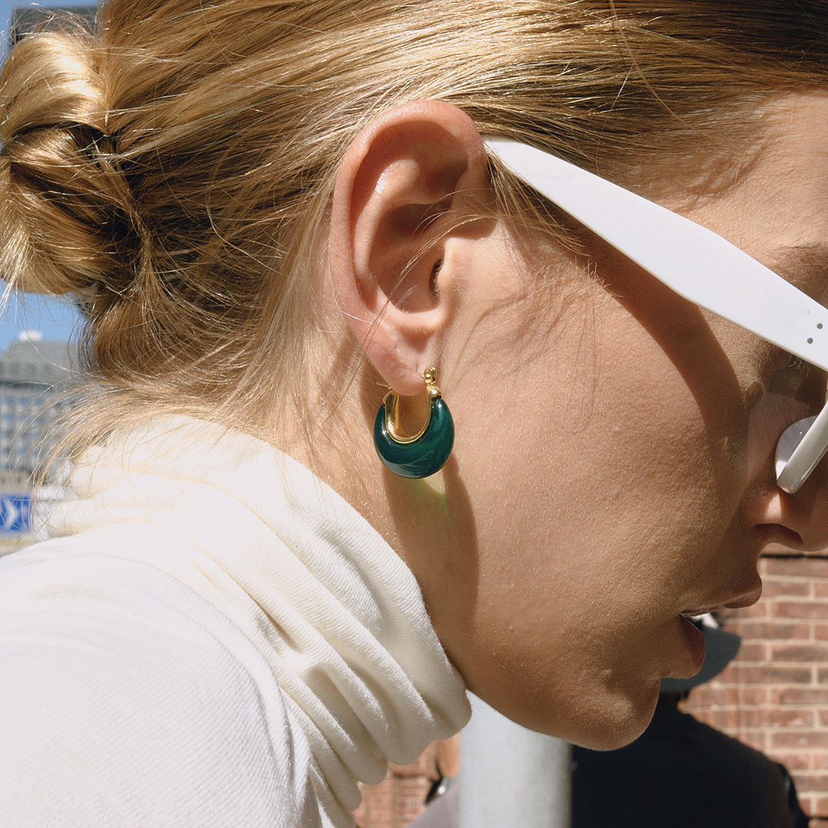 Close-up of a person wearing white sunglasses and turquoise earrings for women with gold accents.
