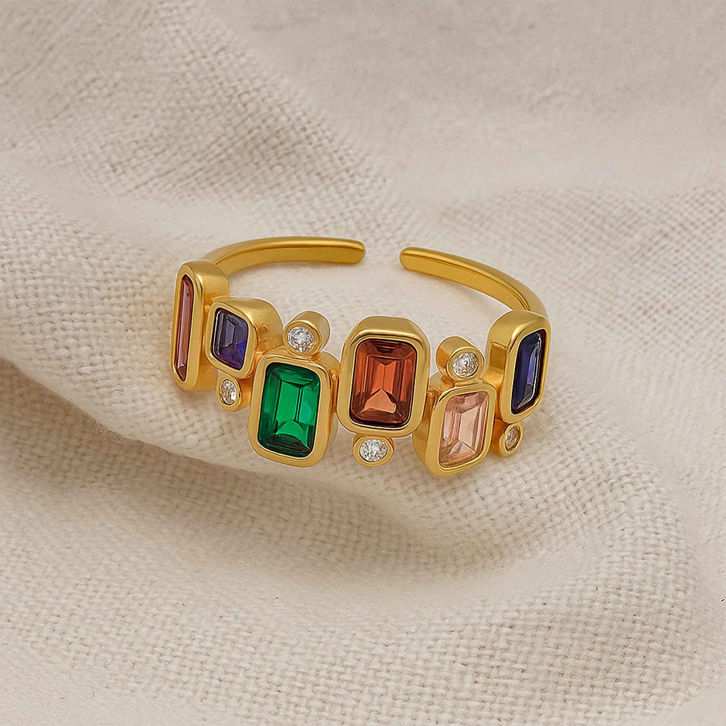 Gold ring with colorful gemstones on a beige fabric background