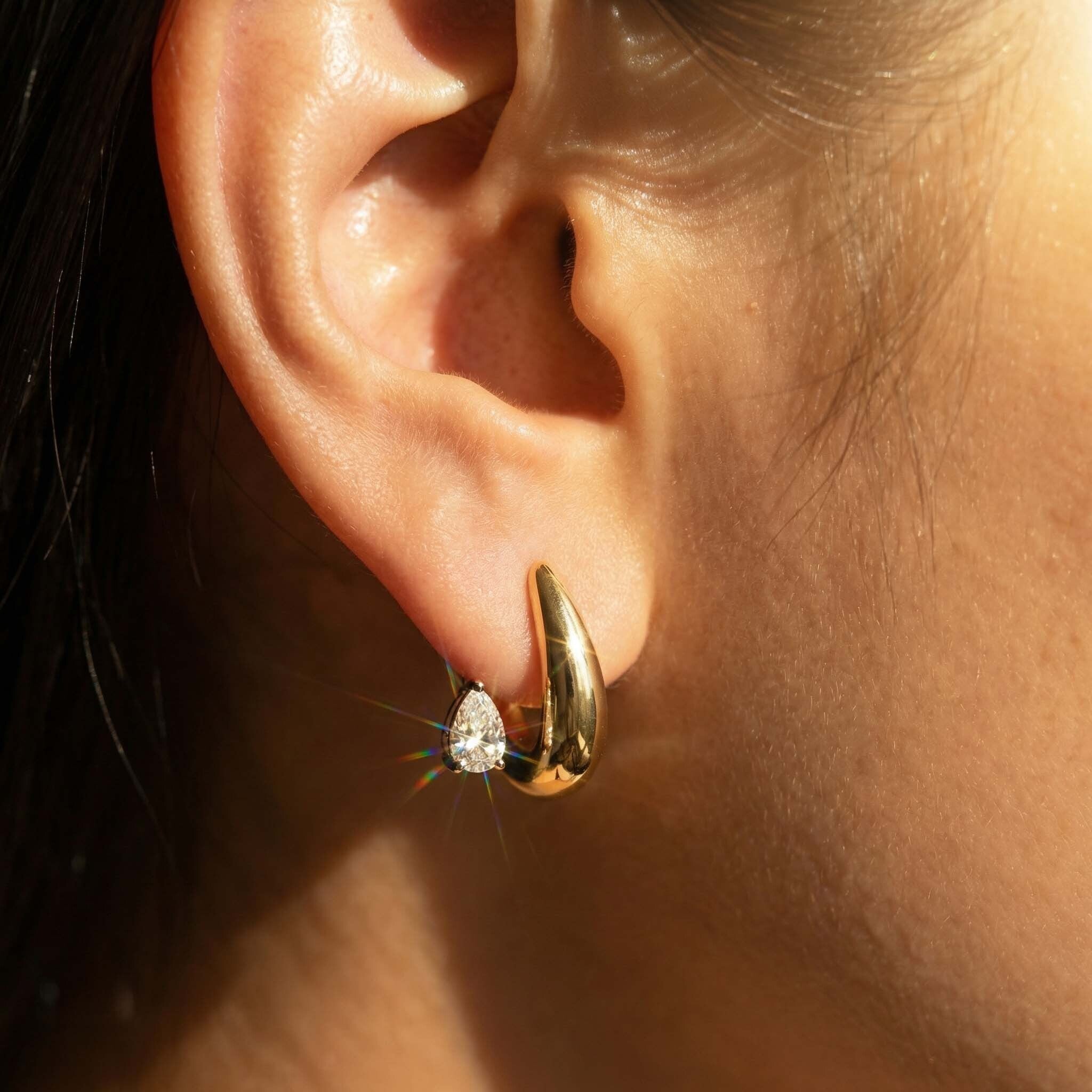 Close-up of a gold hoop earring with a diamond on an ear.