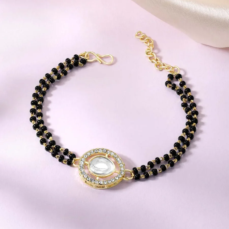 Black beaded bracelet with a gold clasp on a pink background