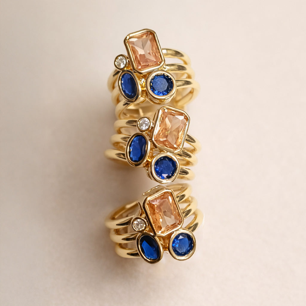  gold ring with blue and peach gemstones on a beige background