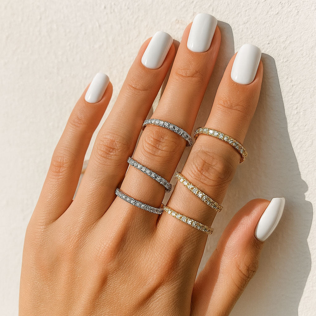 Hand wearing multiple diamond rings with white nail polish on a neutral background
