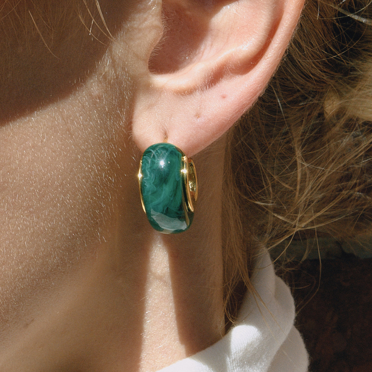 Close-up of an ear wearing a green and gold hoop earring for women