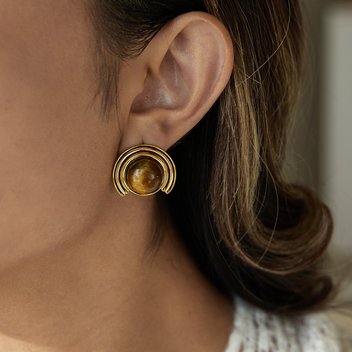 Close-up of a person wearing a gold earring for women  with a central gemstone.